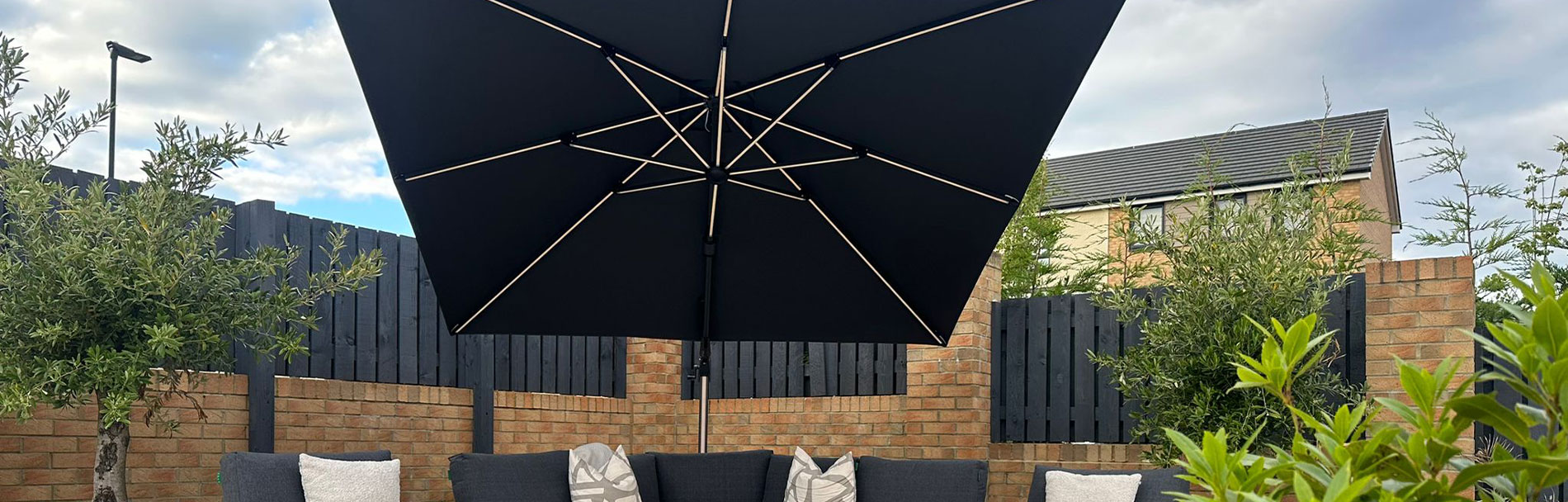 The Astra garden cantilever parasol, in grey with LED lights, in front of garden furniture.