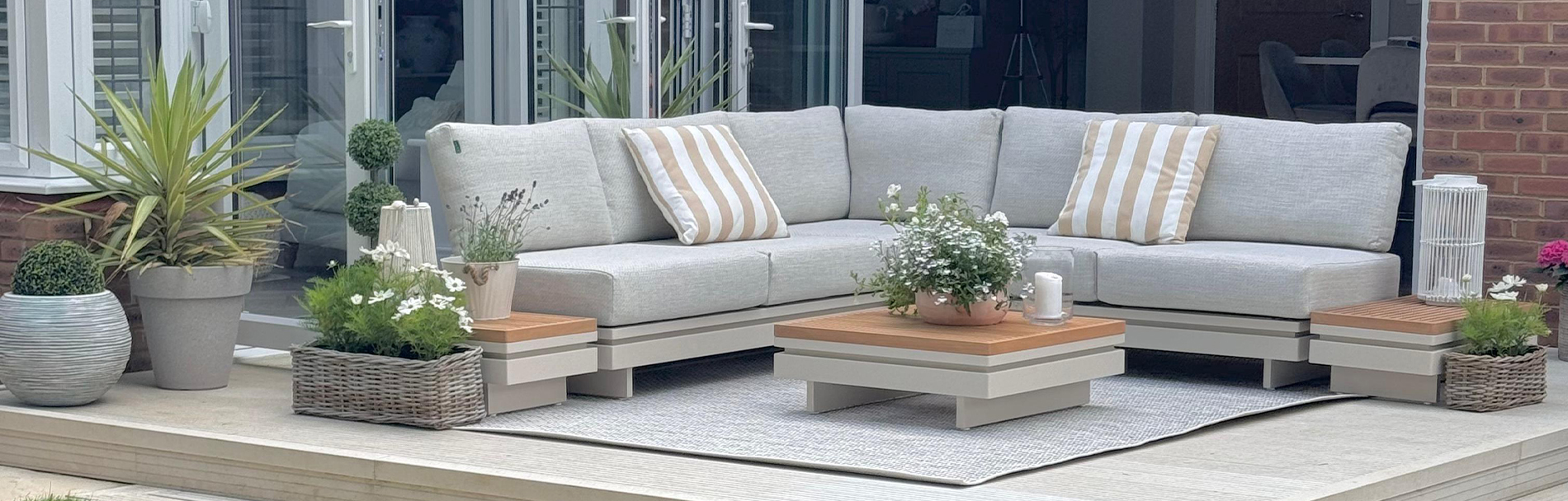 The Bryson garden sofa with cream aluminium and teak accents. Surrounded by plants.
