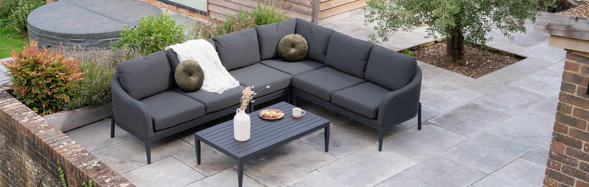 A grey corner sofa on a patio with food and drink on the rectangular coffee table.